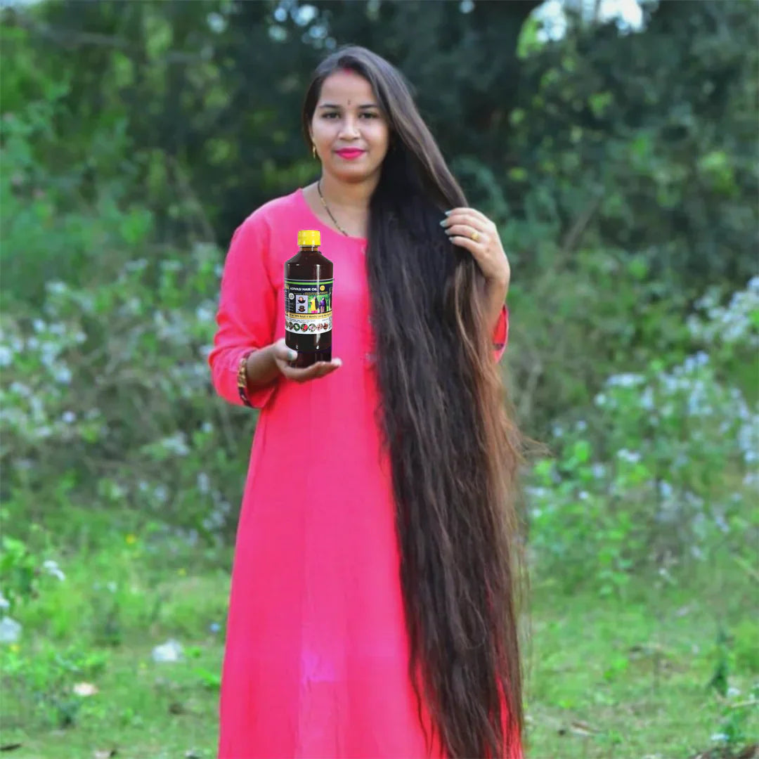 Woman in pink dress with extremely long dark hair holding a bottle of hair oil outdoors